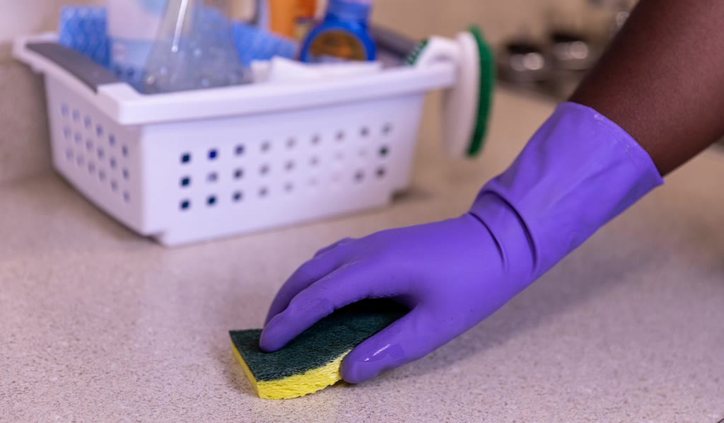 Gloved hand wiping down a kitchen bench